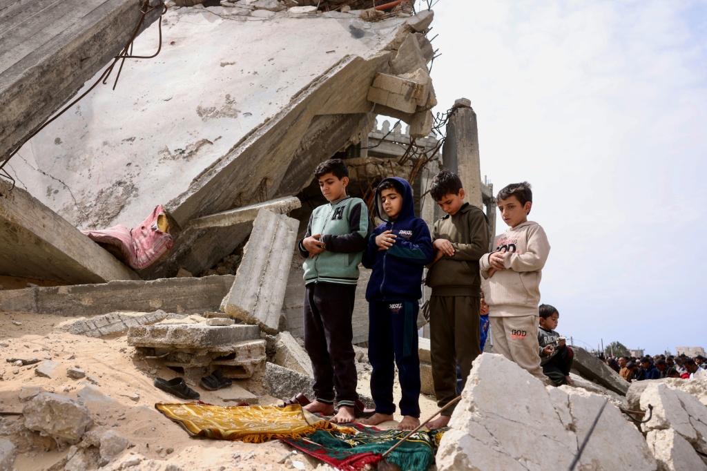 فتية فلسطينيون يؤدون صلاة الظهر في الجمعة الأخيرة من شهر رمضان المبارك، خارج مسجد الطالباني الذي دمره الجيش الإسرائيلي في خان يونس، جنوب قطاع غزة، في 13 آذار/مارس 2026 (ا ف ب) 