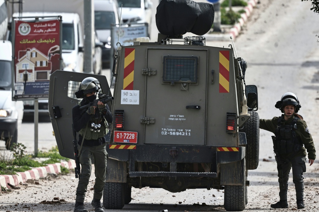 جنود إسرائيليون يقفون قرب مركبتهم العسكرية بينما يمنعون فلسطينيين من المرور، فيما تهدم جرافات عسكرية إسرائيلية منازل يملكها فلسطينيون في قرية شقبا غرب مدينة رام الله في الضفة الغربية المحتلة، في 21 كانون الثاني/يناير 2026 (ا ف ب)