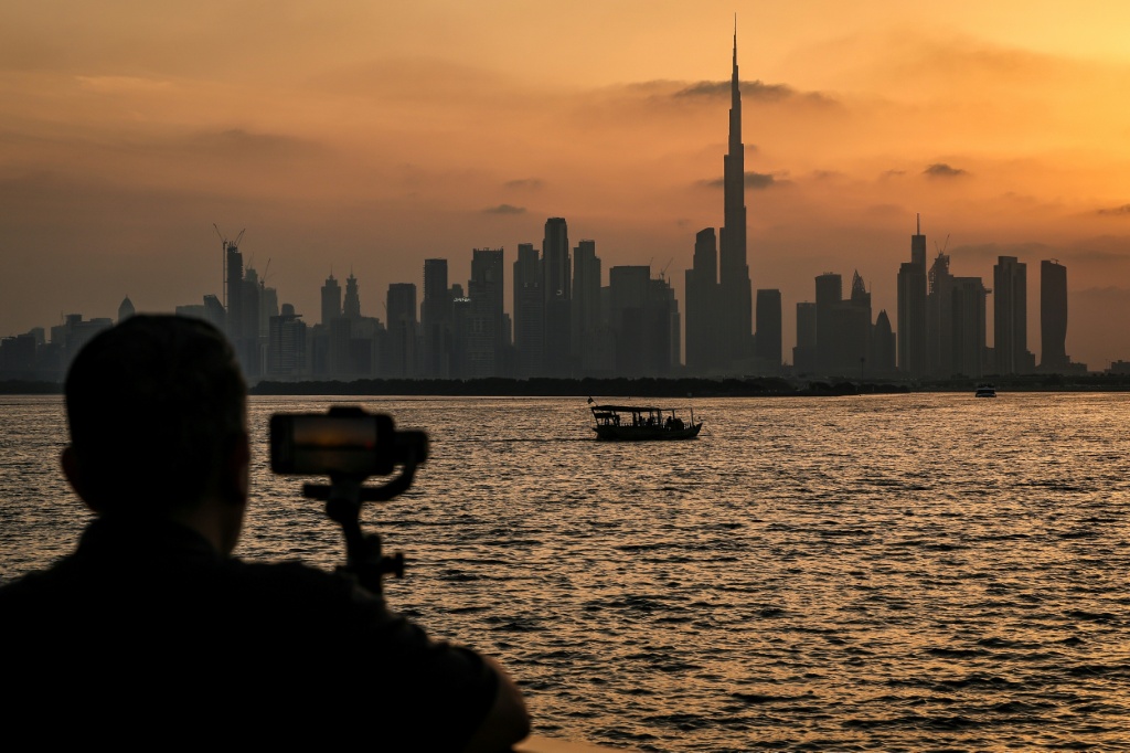 رجل يقف في خور دبي ممسكاً بهاتف ذكي أمام أفق دبي، حيث يظهر برج خليفة، أطول مبنى في العالم، في 3 نيسان/أبريل 2026. (ا ف ب)