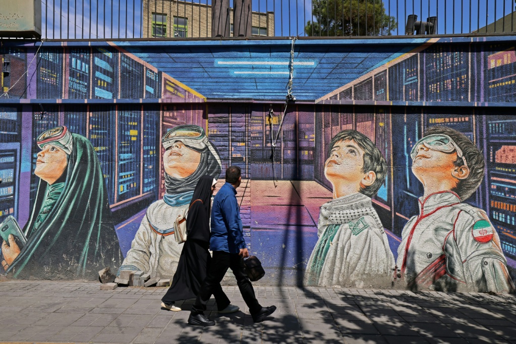 أشخاص يمرّون بمحاذاة جدارية على جانب الطريق في طهران في 12 نيسان/أبريل 2026 (ا ف ب)