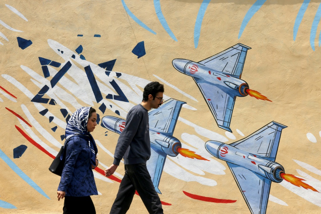 إيرانيون يمرّون من أمام رسم جاري مناهض للولايات المتحدة وإسرائيل في طهران بتاريخ 21 نيسان/أبريل 2026 (ا ف ب)