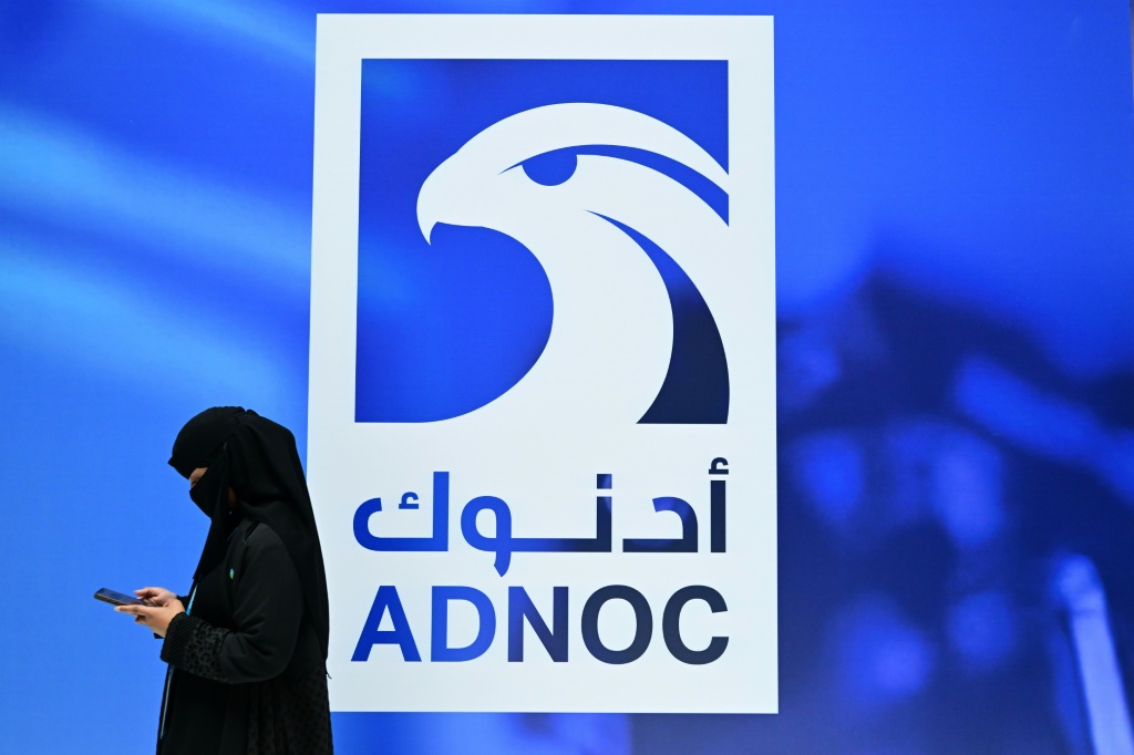 امرأة خليجية تتفقد هاتفها المحمول قرب شعار شركة أدنوك خلال معرض ومؤتمر أبوظبي الدولي للبترول 