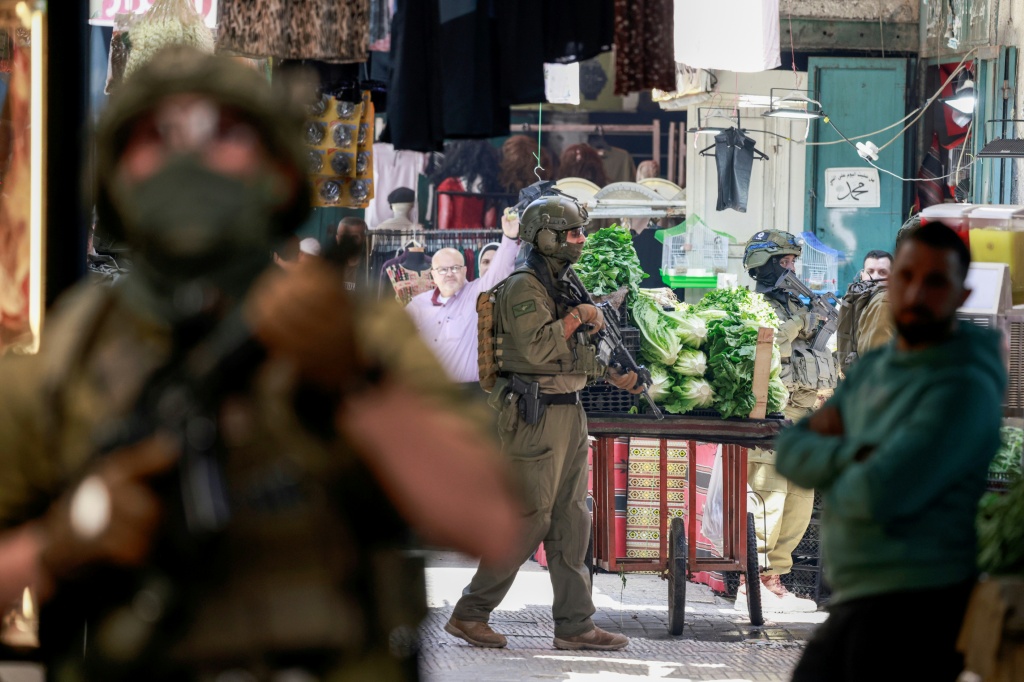 باعة فلسطينيون ينظرون إلى جنود إسرائيليين يقومون بدوريات في السوق بالبلدة القديمة في نابلس في شمال الضفة الغربية المحتلة في 27 نيسان/أبريل 2026 (ا ف ب)