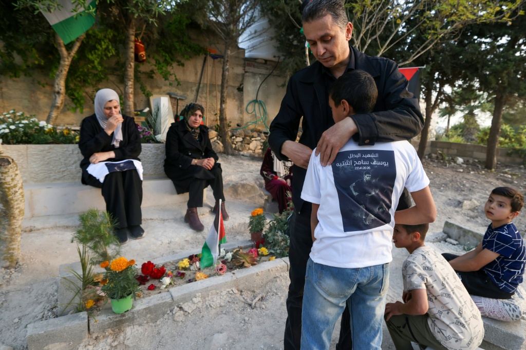 الفلسطيني سامح اشتية والد الطفل يوسف اشتية الذي قُتل برصاص جندي إسرائيلي في 23 نيسان/أبريل 2026، يحتضن ابنه الأصغر خلال زيارتهم لقبر يوسف في 12 أيار/مايو 2026 (ا ف ب)