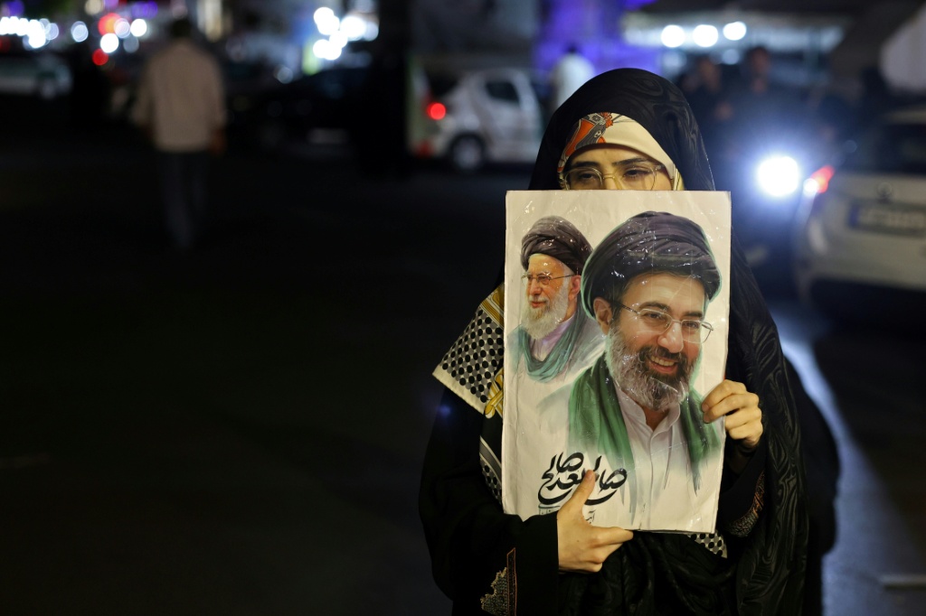امرأة تحمل صورة للمرشد الأعلى الإيراني آية الله مجتبى خامنئي وسلفه ووالده الراحل آية الله علي خامنئي خلال تظاهرة مناهضة للولايات المتحدة وإسرائيل في ساحة هفت تير بطهران في 17 أيار/مايو 2026 ( اف ب)