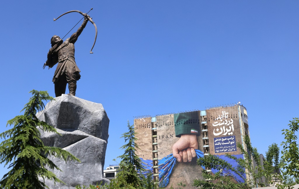 تمثال لشخصية من الأساطير الفارسية في طهران بجانبه لافتة ضخمة تمثل مضيق هرمز مع عبارة "إلى الأبد بيد إيران" في 25 أيار/مايو 2026 (ا ف ب)