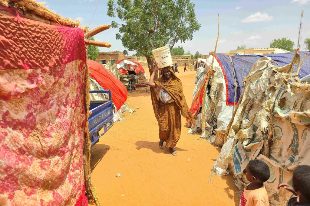 امرأة سودانية تحمل على رأسها حاوية بلاستيكية تحوي ماء في مخيم الرحمانية للنازحين قرب مدينة الأبيّض في إقليم جنوب كردفان في 25 حزيران/يونيو 2026 (ا ف ب)