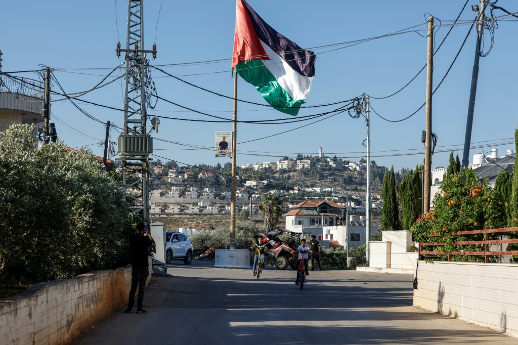 شارع في ترمسعيّا حيث يظهر العلم الفلسطيني شمال رام الله في الضفة الغربية المحتلة فيما تظهر مستوطنة شيلو في الخلفية بتاريخ 28 حزيران/يونيو 2026 (ا ف ب)
